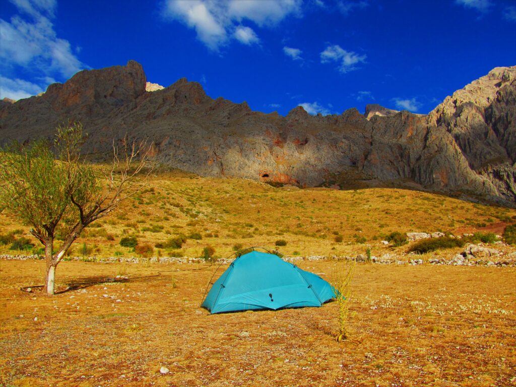 Backpacking in Turkey. A tent sits next to a lone tree. In the background is a mountain range.